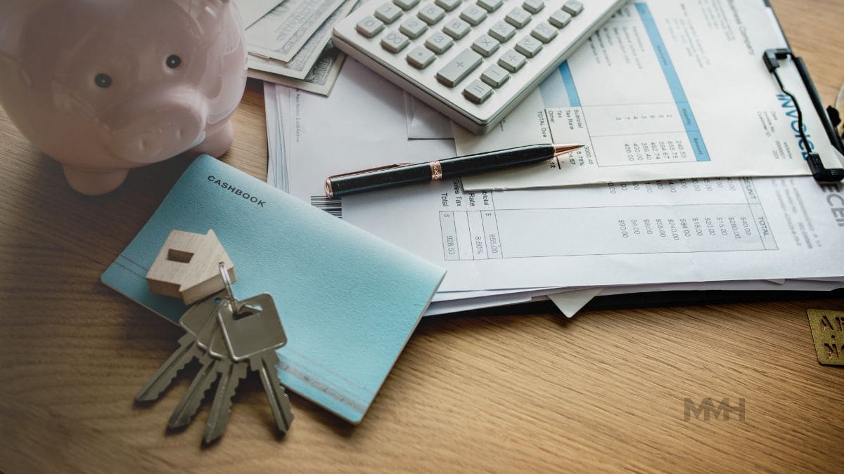A flat lay image showing a piggy bank, cash, a calculator, documents, a pen, a cashbook, and house keys, representing financial matters like mortgages.