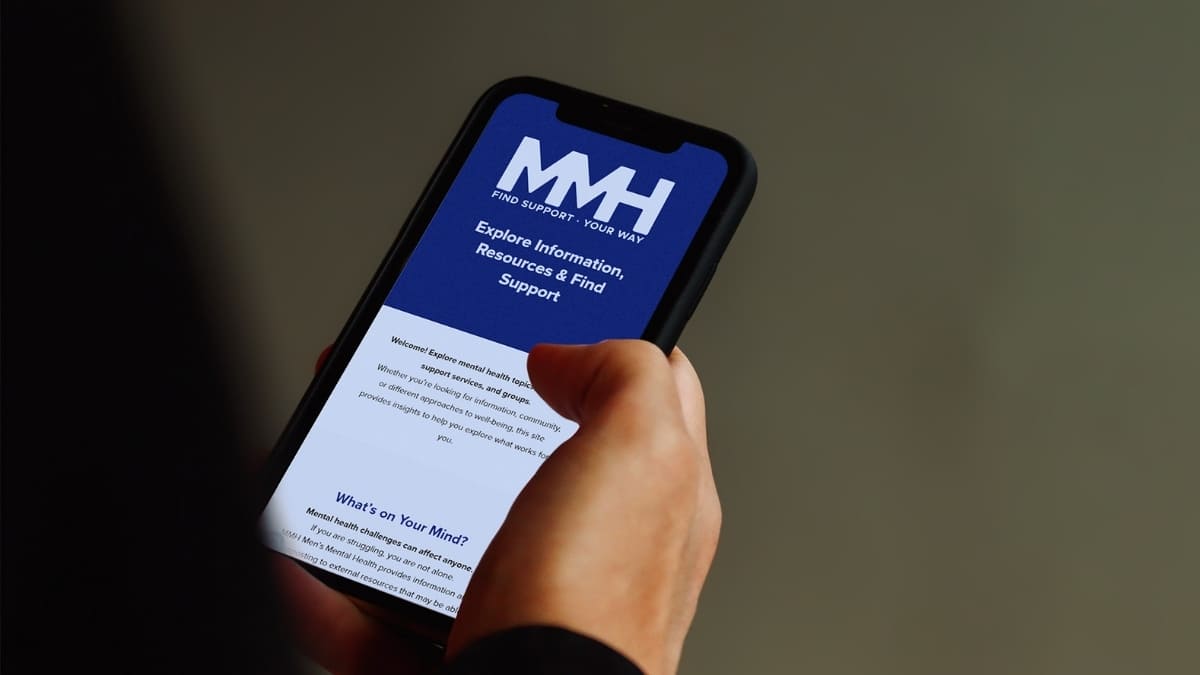 Exploring Mental Health Support on MMH Person browsing the MMH Men’s Mental Health website on a smartphone to find support and resources.