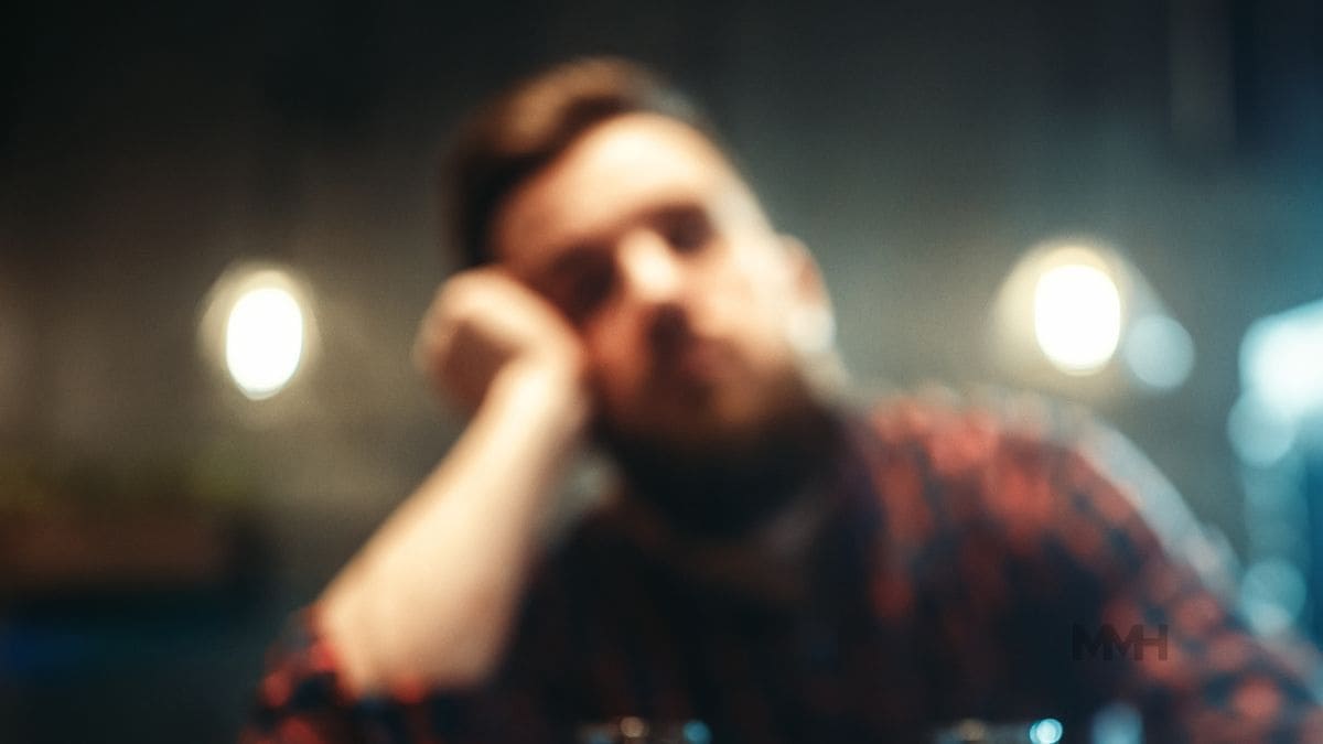 A blurred image of a tired man sitting at a bar, representing the emotional toll and lifestyle impact of alcohol abuse.