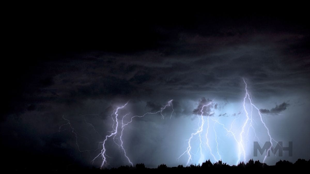 A dark sky with lightning bolts striking above a forest silhouette, symbolising emotional overwhelm and the unpredictable nature of depression triggers in men.