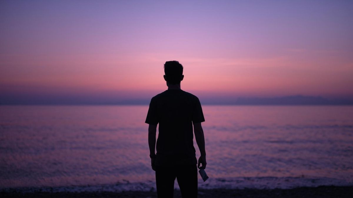 A man standing by the sea at dusk reflecting on loss and grief.