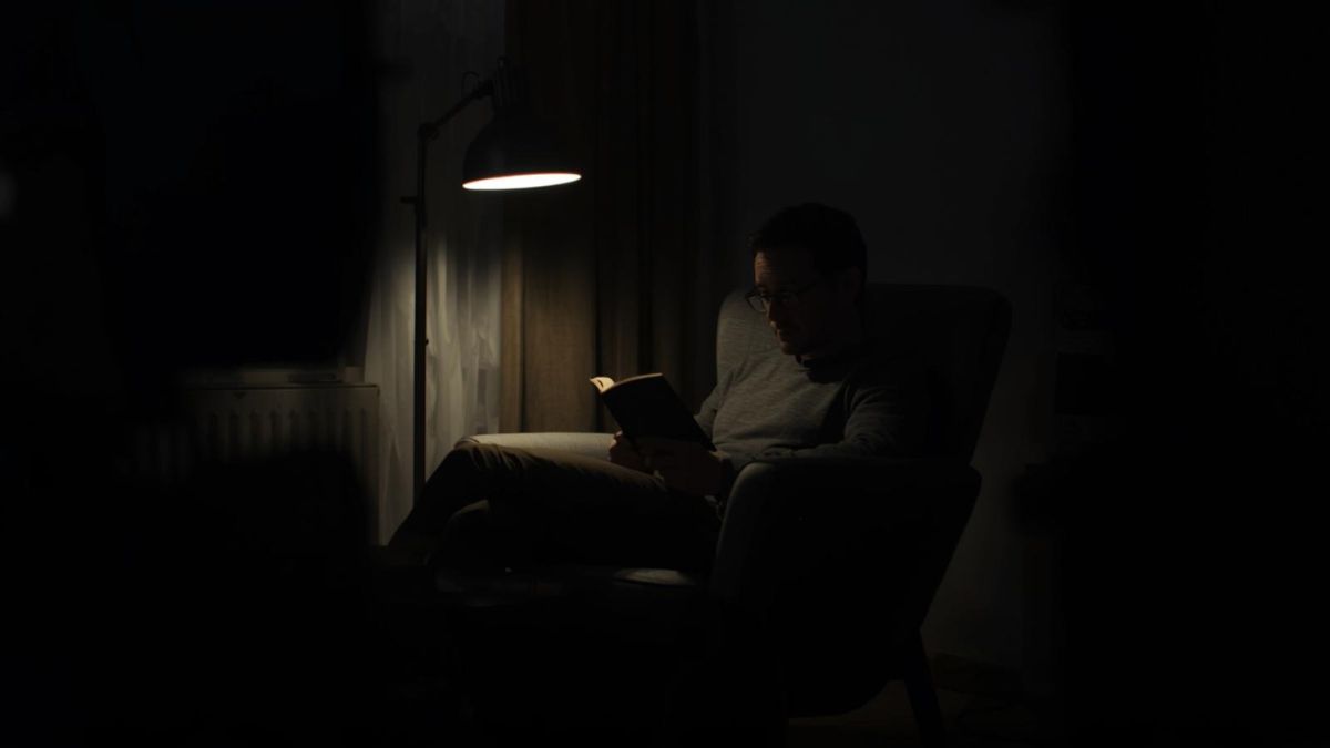 A man sitting alone in a dark room reading, symbolizing loneliness.