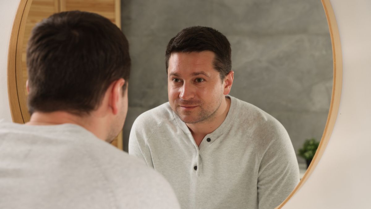A man looking in the mirror adjusting his tie, building confidence.