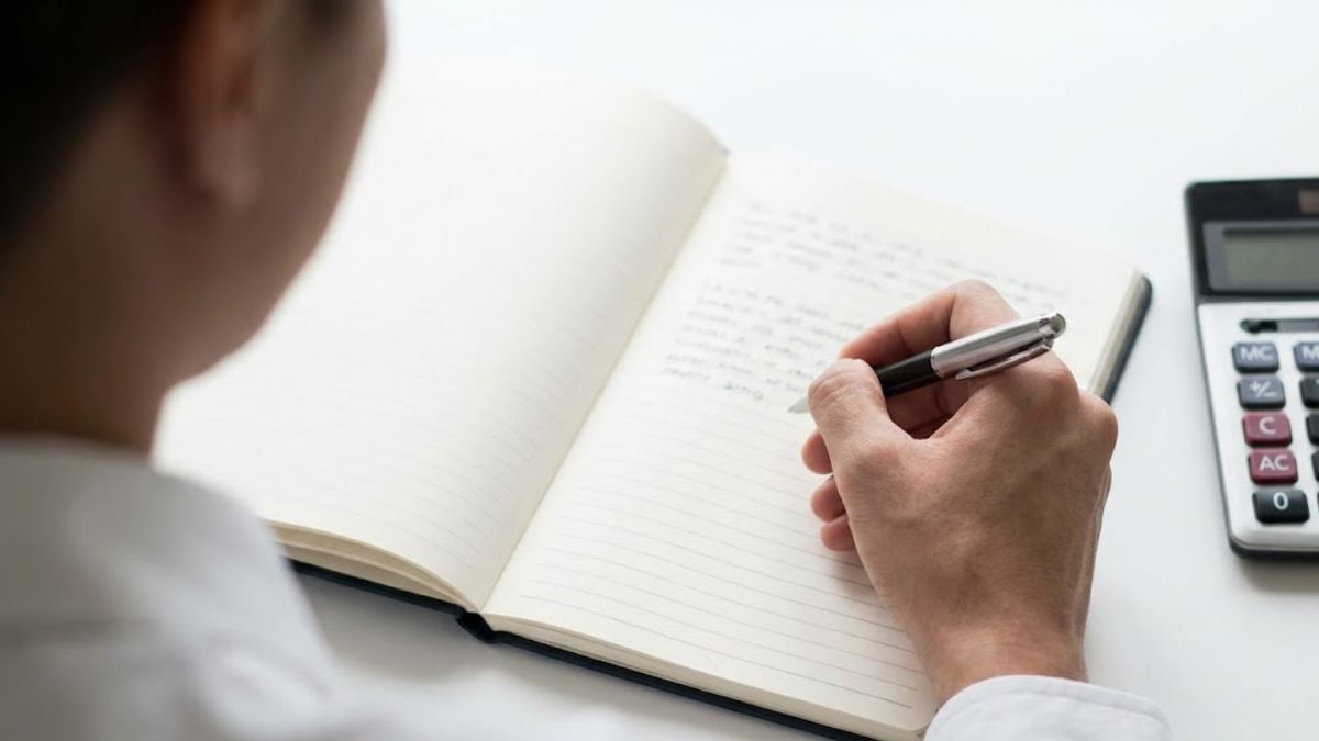 A person writing in a notebook with a calculator nearby, symbolizing creating a financial plan and taking control of mental health.