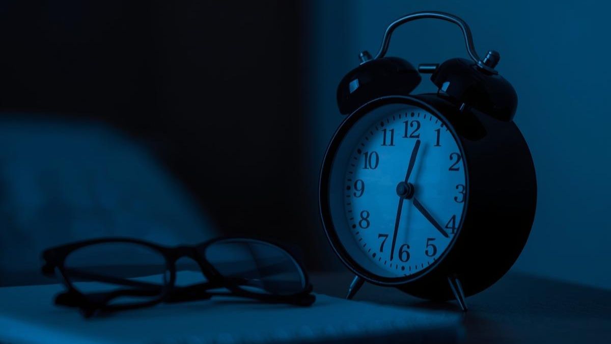 An analogue clock on a bedside table in a dimly lit room representing sleep patterns.