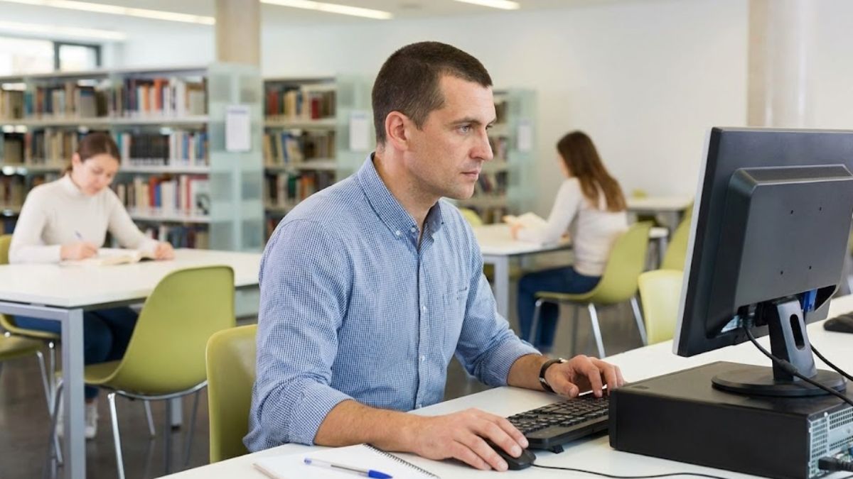 A man using a computer in a public library, a practical step towards finding work and housing to break the cycle of homelessness.