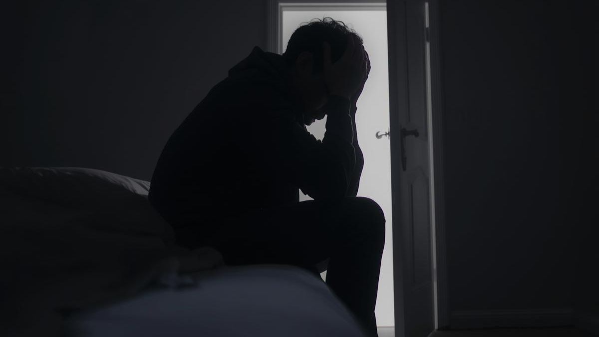 A man sitting in a dark room with a door opening to light, symbolizing hope and support for abuse victims.
