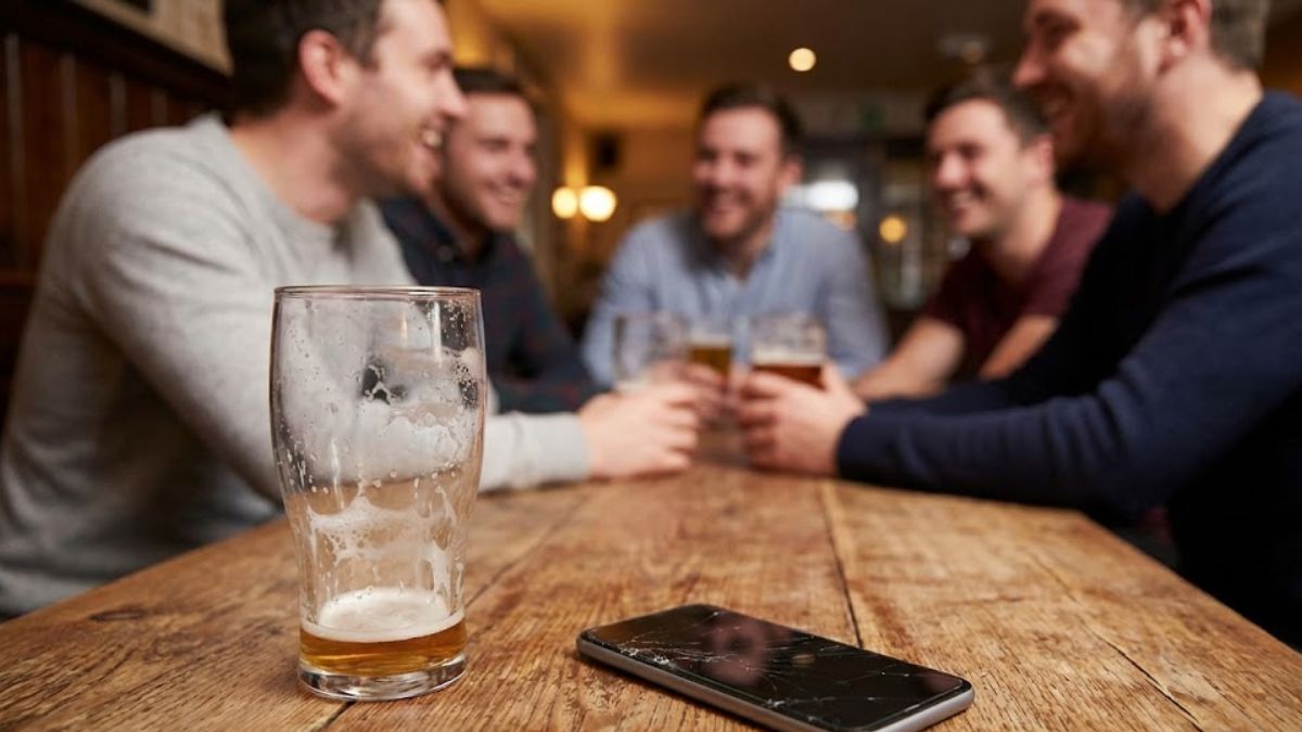 A lonely pint glass in the foreground with a blurred group of men socialising in the background.