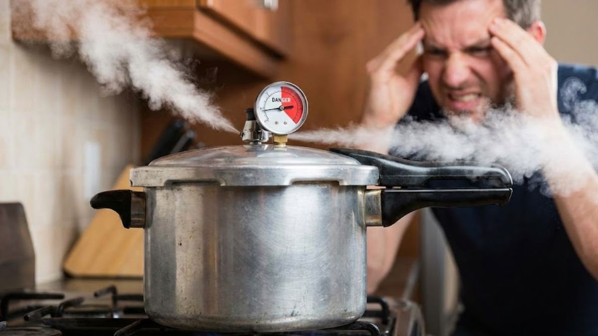 A stovetop pressure cooker emitting steam with its gauge in the red "danger" zone, symbolizing built-up psychological pressure, with a stressed man clutching his head in the blurred background.