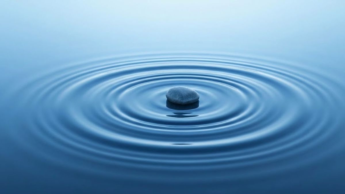 A single stone dropped into calm, blue-toned water, creating concentric ripples that spread outward.