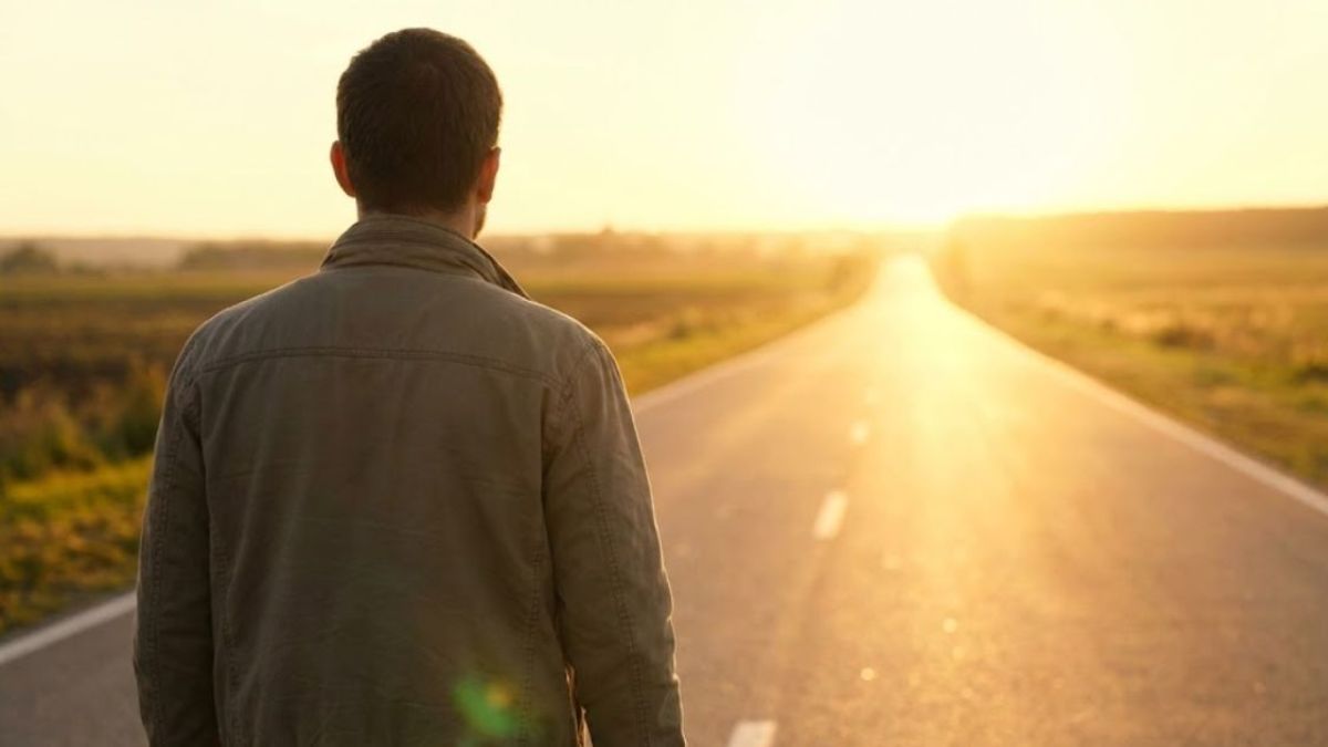 A man seen from behind walking down a long, sunlit road towards a sunrise, symbolizing a fresh start and leaving burdens behind.